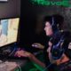 Jogadores em um café de eSports no Brasil usando headsets enquanto competem em jogos online.